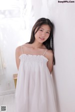 A woman in a white dress leaning against a wall.